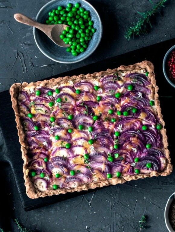 Zwiebelkuchen vegan eckig mit roten Zwiebeln belegt und Erbsen bestreut