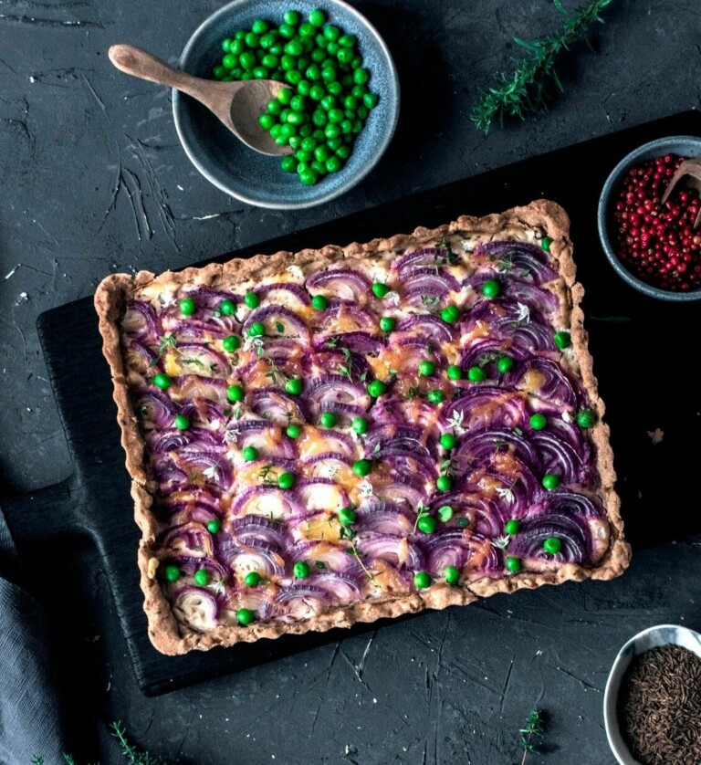Zwiebelkuchen vegan eckig mit roten Zwiebeln belegt und Erbsen bestreut
